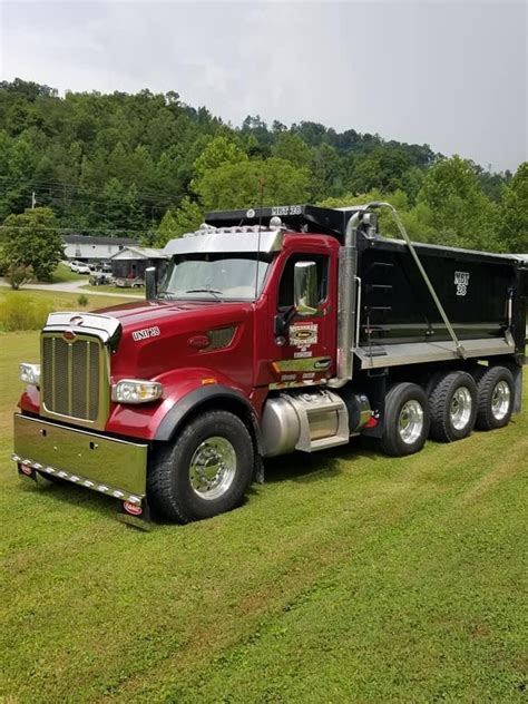 a large red dump truck parked on top of a grass covered field with trees in the background