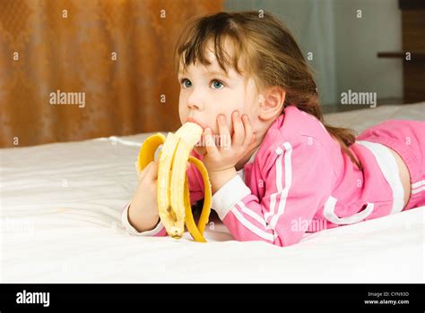 Cute Little Girl se come un plátano en la cama en casa Fotografía de ...