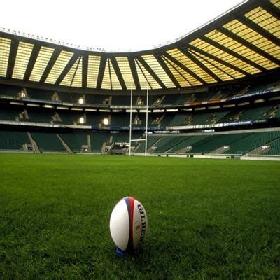 a rugby ball sitting on top of a green field in front of a large stadium