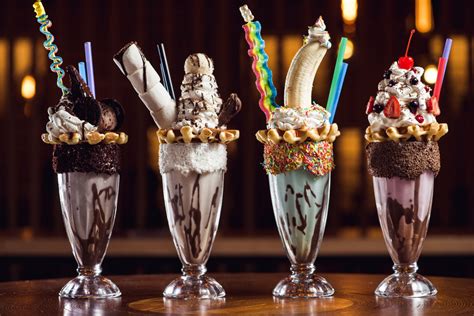 Four unique giant milk shakes in row on a wooden table. - MyStart