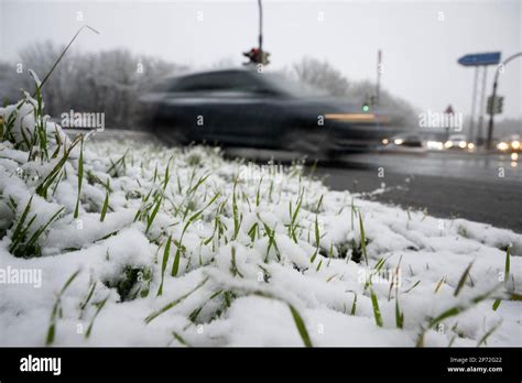 08 March 2023, Hesse, Gießen: A car drives past snow-covered grass. An official warning of ...