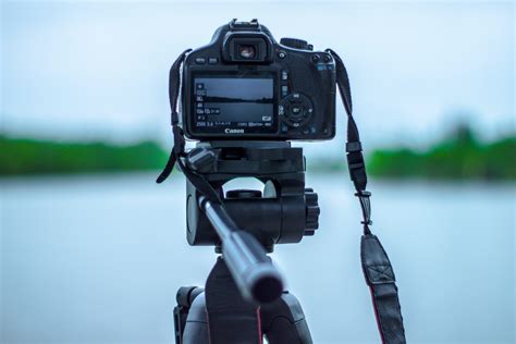Selective Focus Photo of Black Canon Camera on Tripod Stand in Front of Body of Water Photo ...