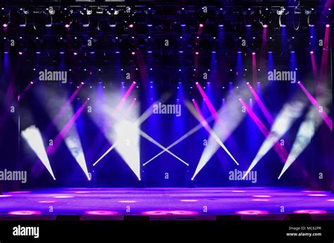 Illuminated empty concert stage with haze and rays of red, purple and blue light. Background for ...