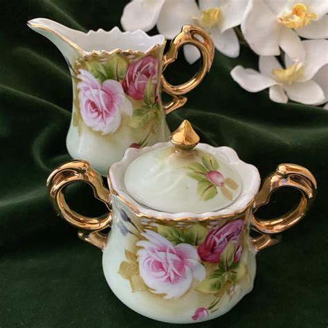 two porcelain teapots with flowers on them sitting next to some white orchids