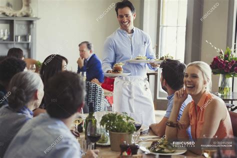 Smiling waiter serving food to friends dining at restaurant table — selective focus, lifestyle ...