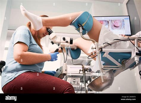 Side view of gynecologist using colposcope while examining woman in gynecological clinic. Female ...