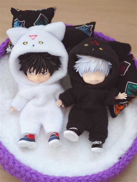 two small dolls are sitting in a purple bowl with white fur and black cats on it