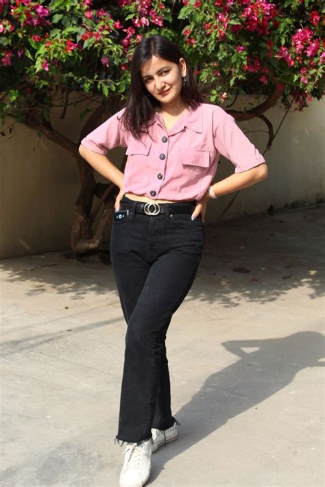 a woman in black pants and pink shirt posing for the camera with her hands on her hips