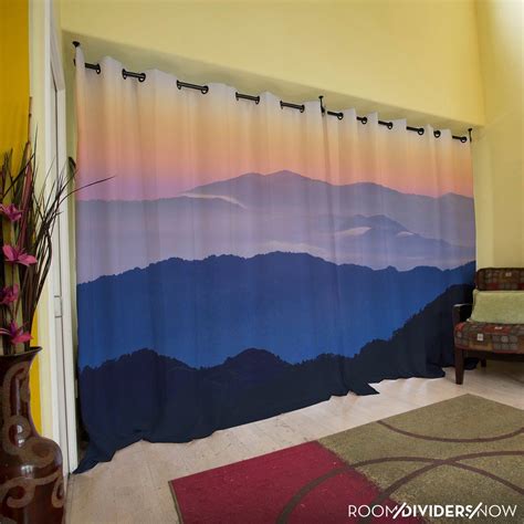 a living room with a couch, chair and window curtain in front of the mountains