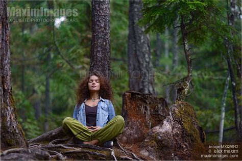 Photo of Young woman resting meditating in forest sitting against tree trunk in nature scenery ...