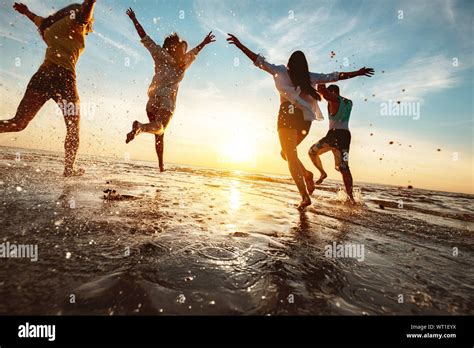 Four happy friends at sunset beach party runs to water Stock Photo - Alamy