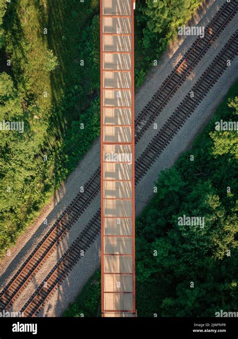 A vertical aerial view of a bridge hanging above train tracks inside a forest Stock Photo - Alamy