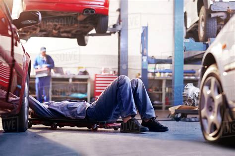 Mechanic under car in auto repair shop - Stock Photo - Dissolve