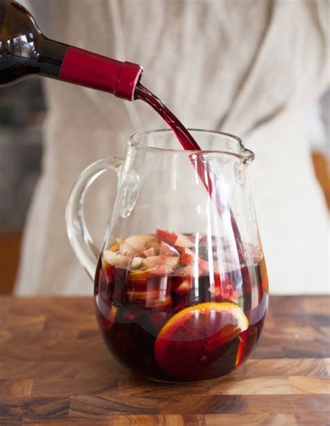 a person pouring red wine into a pitcher filled with fruit