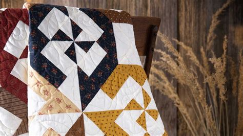 a quilt hanging on the back of a wooden chair next to tall grass and flowers