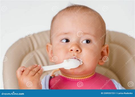 The Child Independently Eats Cottage Cheese with a Spoon Sitting on a Chair on a White ...