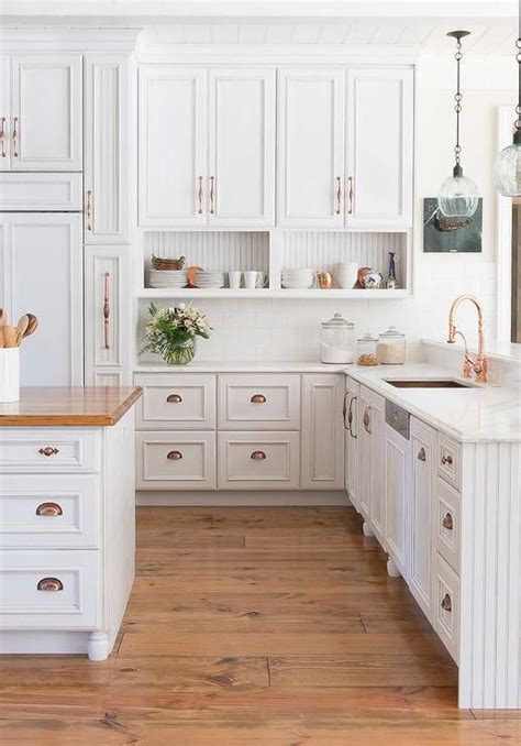 Amazing kitchen features white raised panel cabinets adorned with copper hardware paired with ...