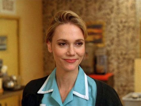 a woman standing in a kitchen wearing a blue shirt and black jacket ...