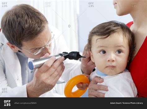 Ear examination. Otoscope being used by a general practice doctor to examine a one-year-old boy ...