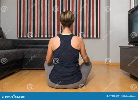 Woman Sitting on Her Back Doing Yoga and Meditating in Her Living Room, Watching a Workout on ...