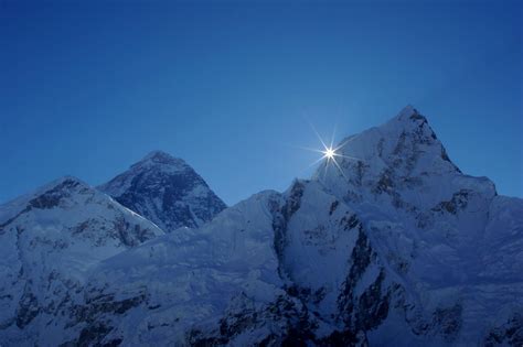 the sun shines brightly above some snow covered mountain peaks in the evening hours,