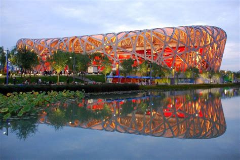 the bird's nest stadium is lit up at night, reflecting in the water