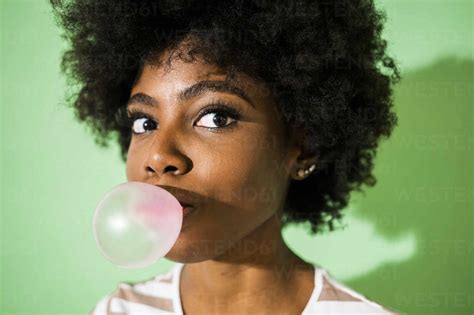 Young woman blowing bubble gum while standing against green background stock photo