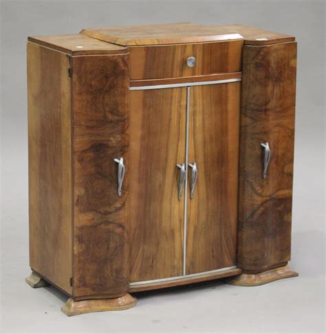 An Art Deco walnut drinks cabinet, the hinged top above four doors, on ...