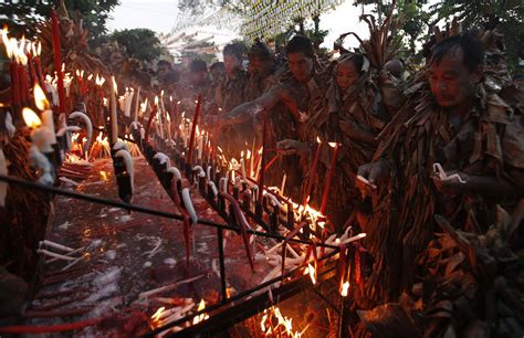 Residents, covered with dried banana leaves and mud, light candles as they take part in a ...