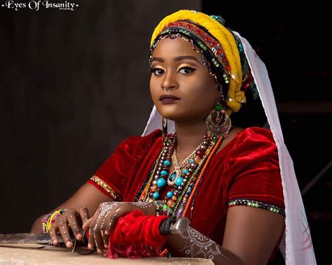 a woman in a red dress and headdress sitting at a table with a knife