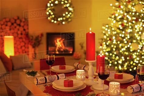 Ambient candles and Christmas crackers on dinner table in living room with fireplace and ...