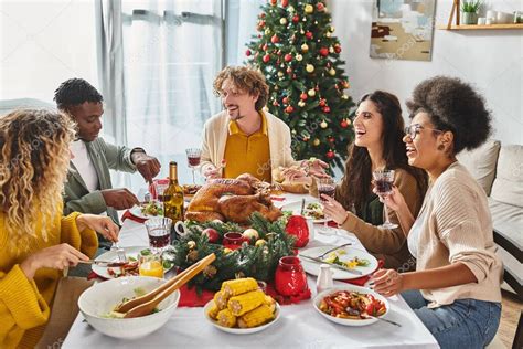 gran familia multicultural teniendo almuerzo festivo y hablando animado con el árbol de Navidad ...