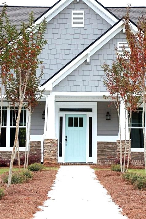 a blue front door and some trees in front of a gray house with white trim