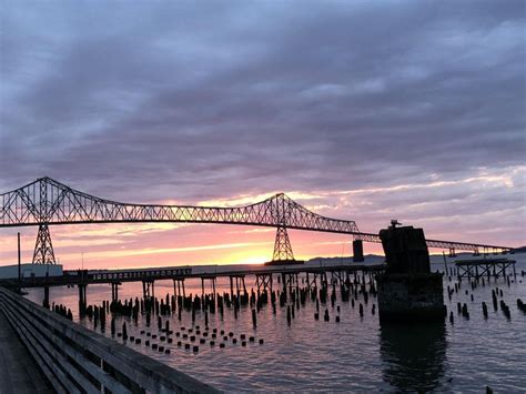 a large bridge spanning over a body of water under a cloudy sky with the sun setting behind it