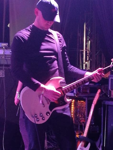 a man in black shirt and hat playing guitar on stage with purple ...