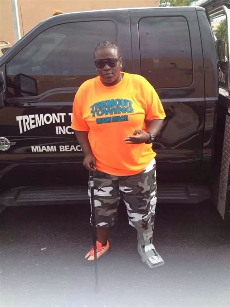 a man in an orange shirt and camo pants stands next to a black truck