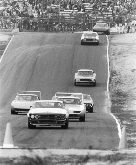 several cars driving on a race track with spectators in the stands watching from behind them