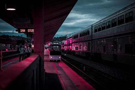 pink light glows on an urban train station as train cars pass, pink ...