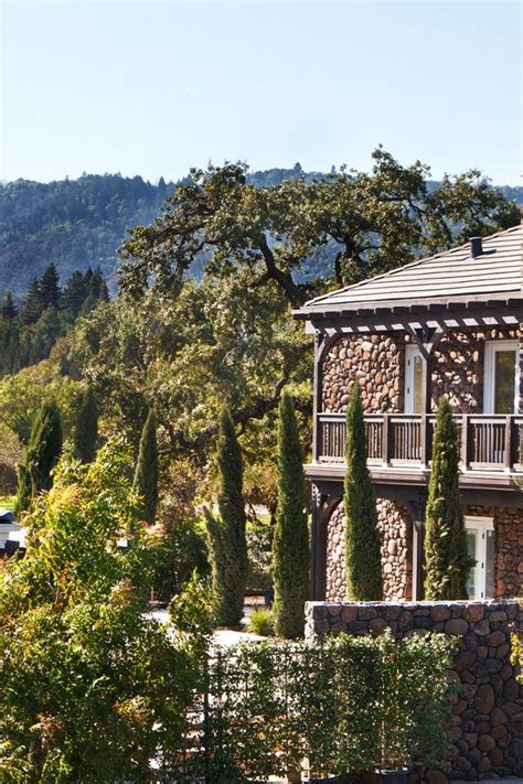 an old house with trees and bushes in the foreground, surrounded by mountains behind it