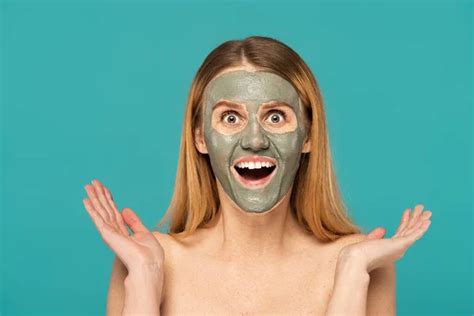 amazed woman with red hair and clay mask on face gesturing isolated on ...