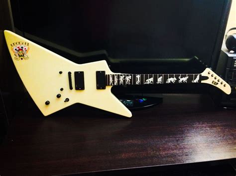 a white electric guitar sitting on top of a wooden desk next to a computer monitor