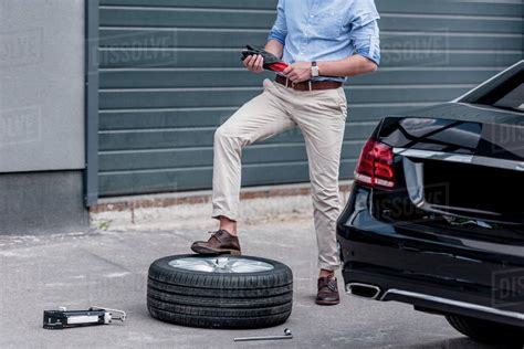 cropped view of young man changing car tire - Stock Photo - Dissolve