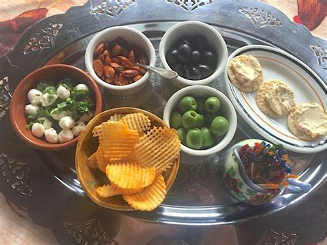 an assortment of snacks are arranged in bowls on a silver platter, along with crackers and olives