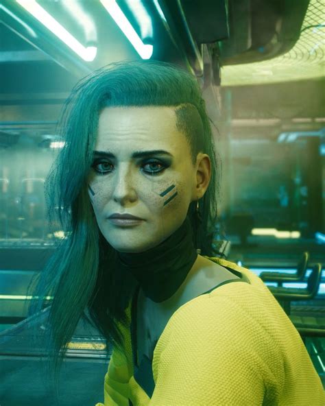 a woman with green hair and makeup looks at the camera in a sci - fi setting