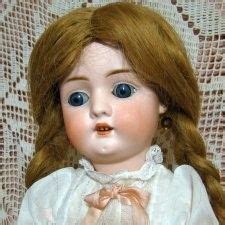 a doll with red hair and blue eyes sitting on a lace tablecloth covered chair