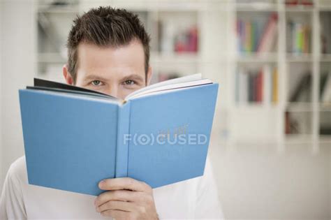 Portrait of playful man holding book in front of face — looking at camera, Focus On Foreground ...