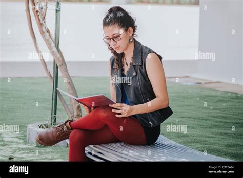 Urban girl sitting on a bench reading a book, Latin girl reading a book outside, concept of a ...