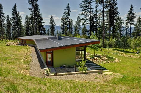 a small green house sitting on top of a lush green hillside next to trees and grass