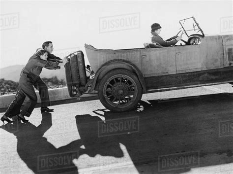 Couple pushing woman in car up hill - Stock Photo - Dissolve