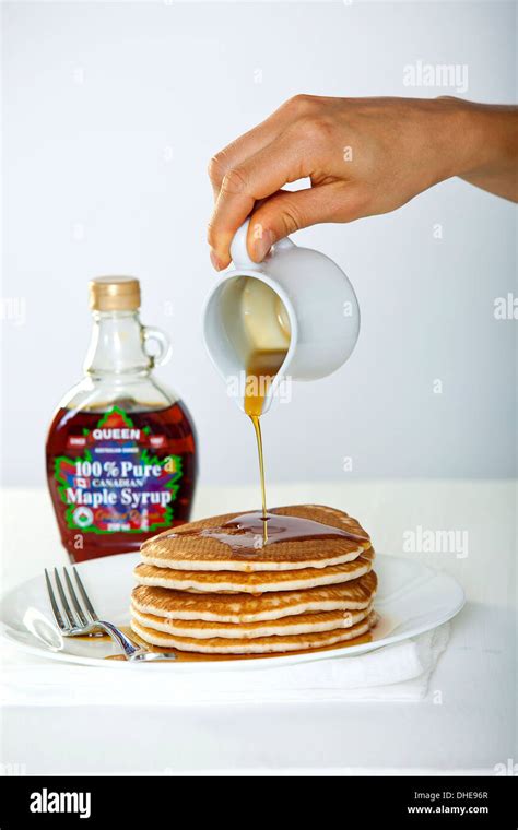 A hand pouring maple syrup from a jug onto a stack of pancakes Stock ...